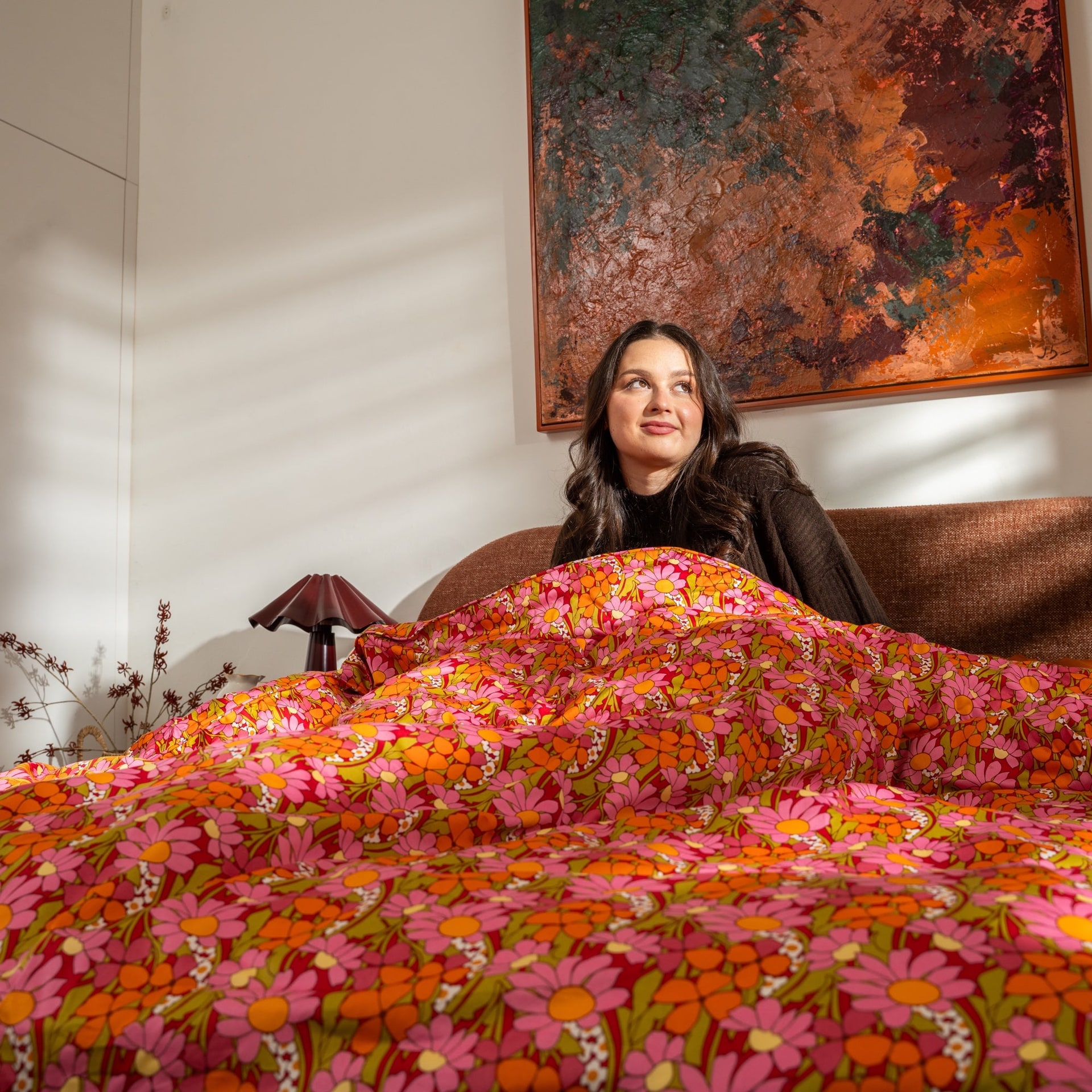 Petal floral bedding in a sunlit bedroom beneath warm abstract art