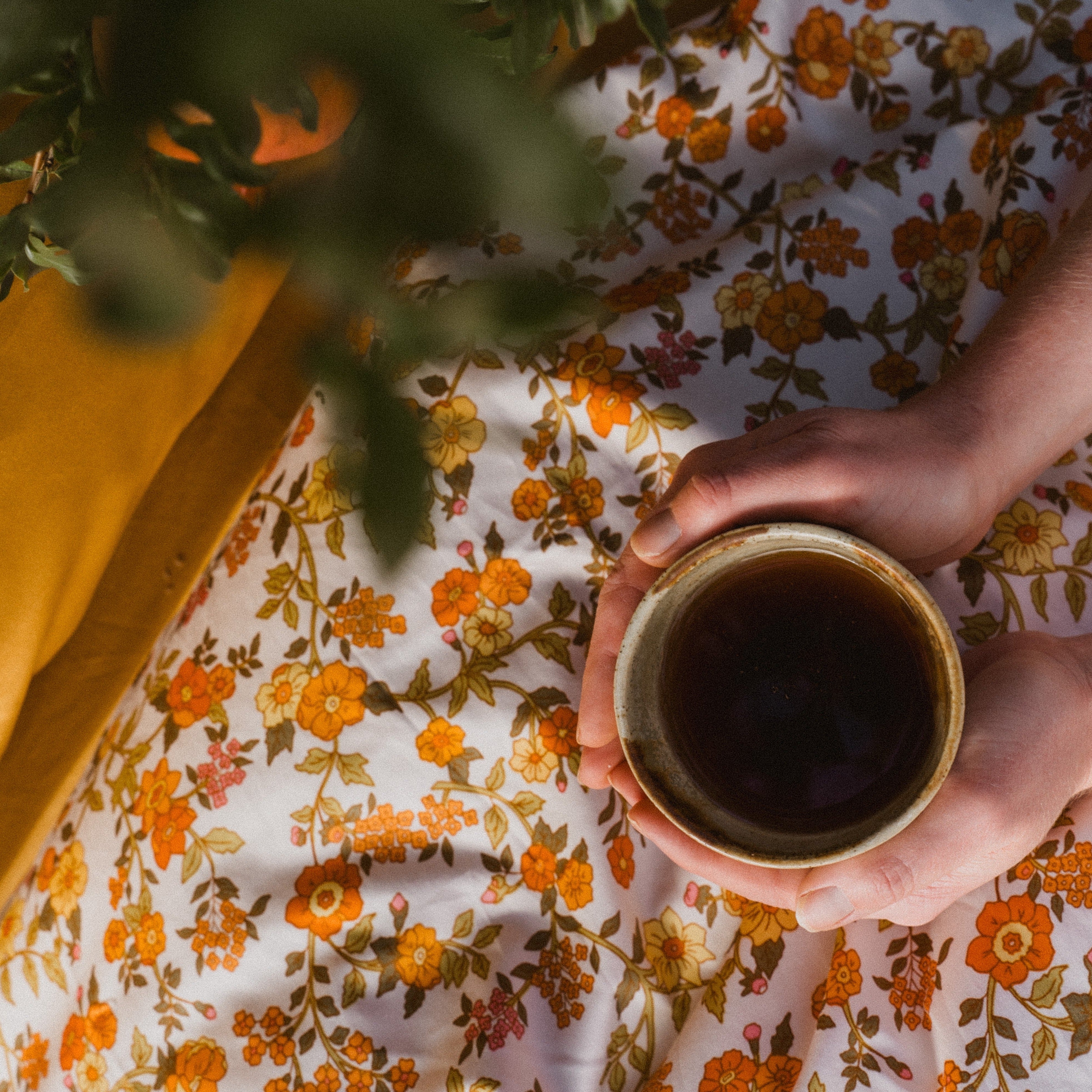 Gorgeous Beddie vintage cotton sheet with a cup of warm tea in a womans hands. It sits well with Honey Mustard coloured bedding. A persimon tree is slightly out of focus on the photo in the forgound