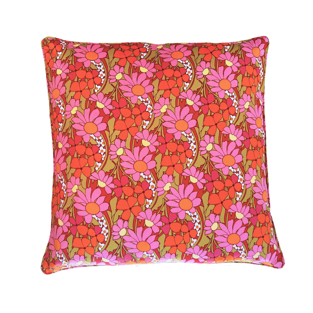 A beautiful square cushion with pink orange petals and yelow circles and khaki green leaves. It is a complex design and they layer over each other in a bright and joyful pattern